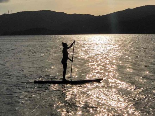 woman paddling boarding at sunset